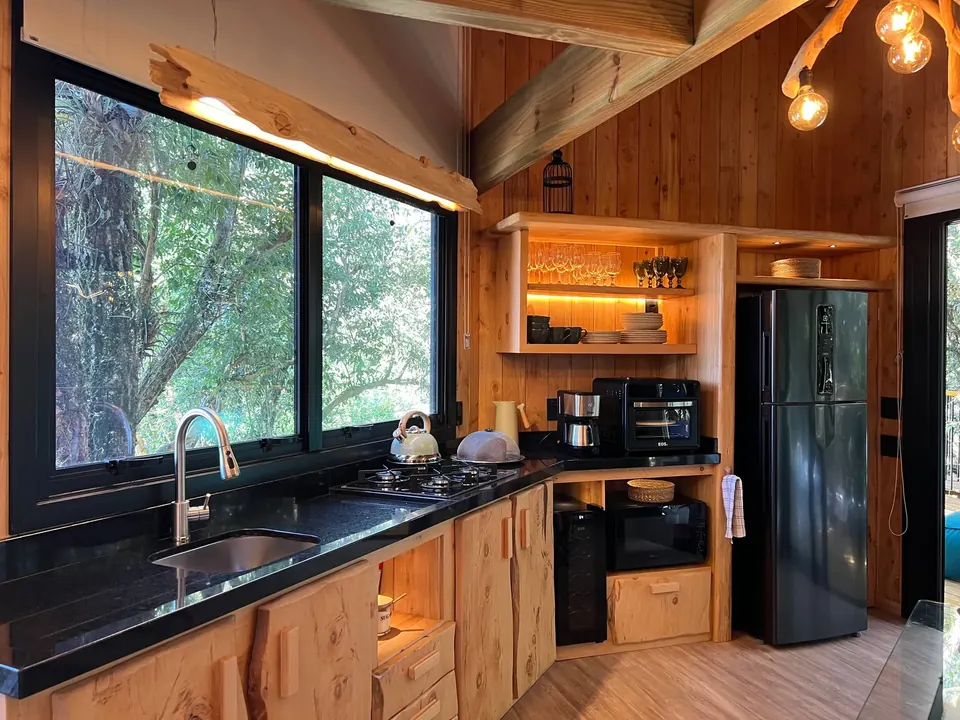 Cozinha com bancada escura e janelas para as árvores