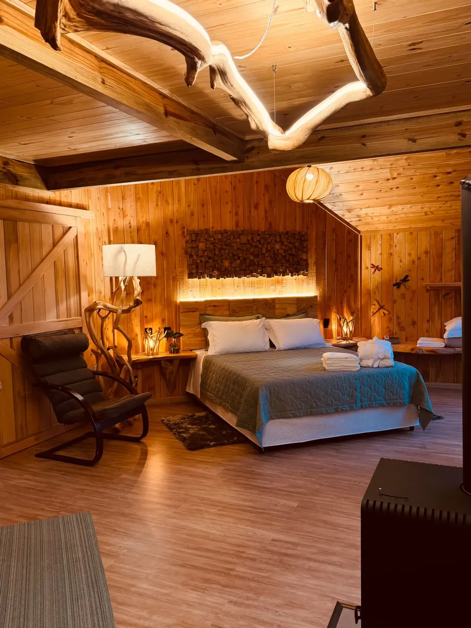 Quarto de casal iluminado, com poltrona e forro de madeira