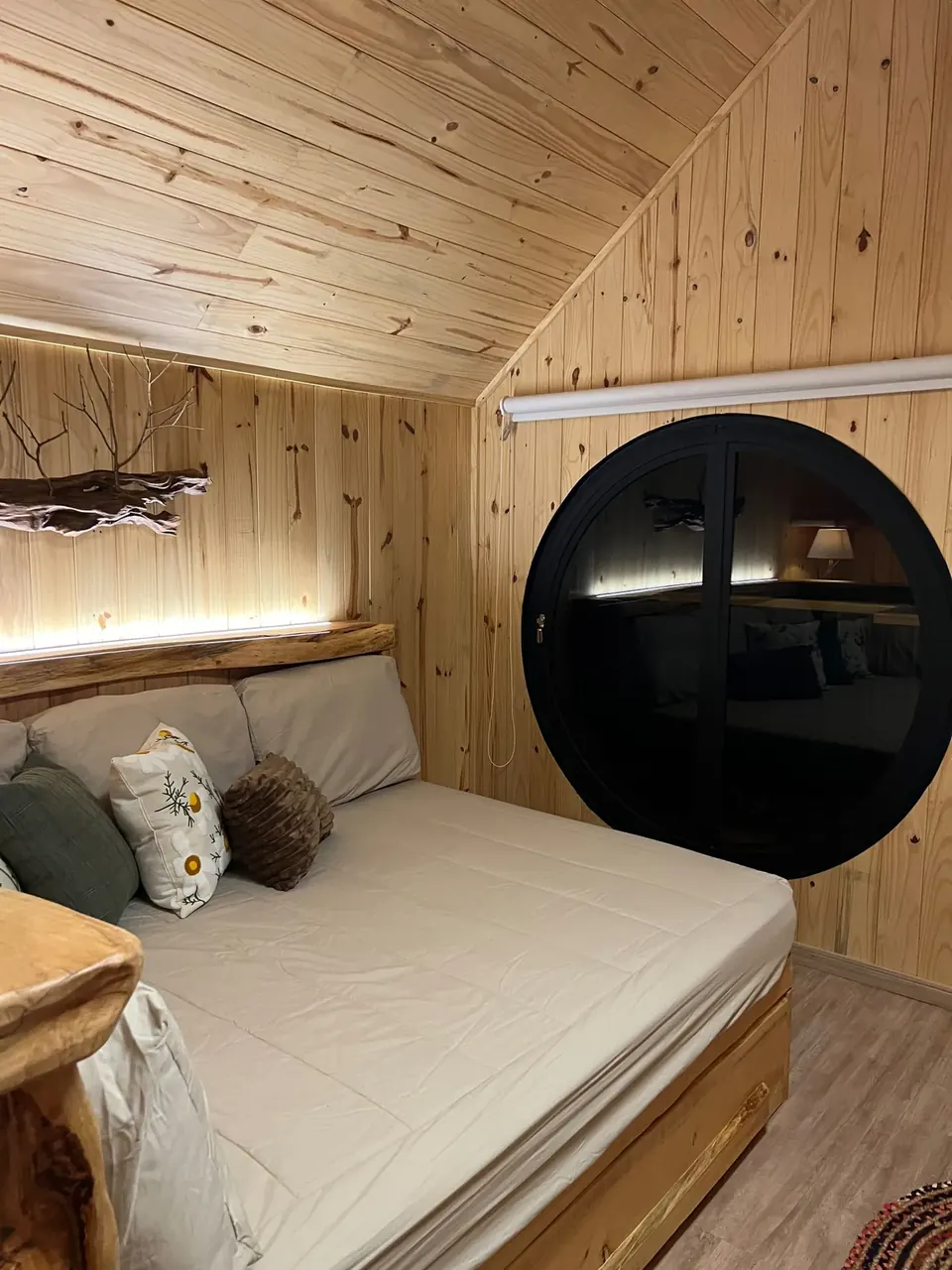 Quarto com cama de casal e janela redonda para o bosque